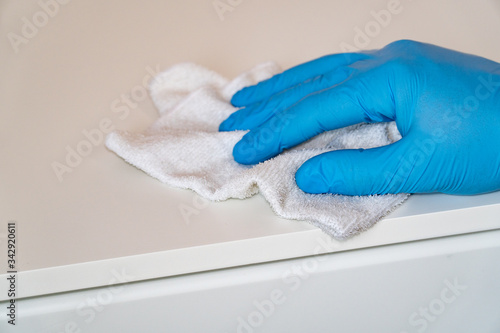 Protective blue gloves washes the furniture on the nightstand with a rag. Prevent the spread of coronavirus and infection COVID-19