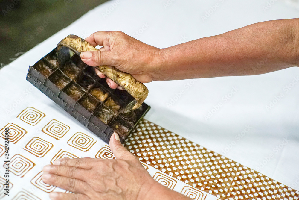 Fototapeta premium Surakarta Indonesia June 4, 2020 : Close up hand on progress make batik with stamp to the white fabric with bokeh background