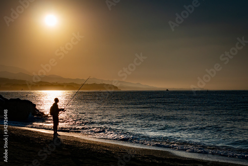 silueta a contraluz de pescador con caña de pescar en amanecer naranja