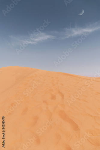 Giant sand dune in the desert and a blue sky with a sungle long cloud and the moon