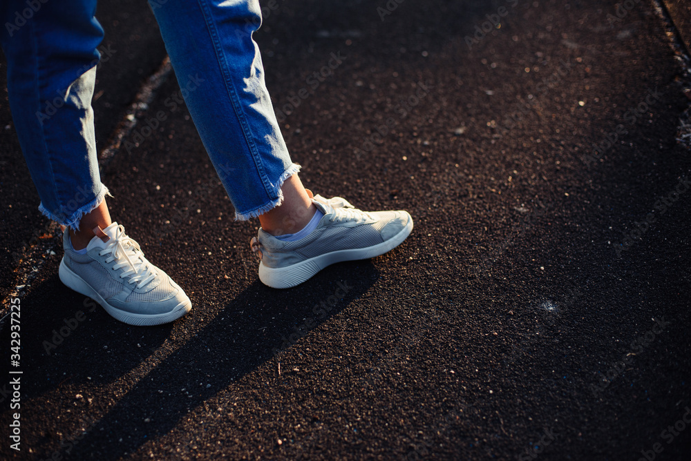 Decide which way to go. Walk rubberized road. Female legs in jeans and gray sneakers. Decide which way to go. Walk rubberized road. Female legs in jeans and gray sneakers.
