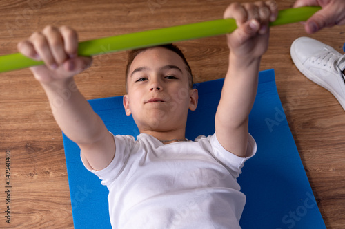 Little boy has musculoskeletal therapy by doing exercises on floor mat. Rehabilitation center.