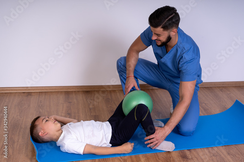 Young physiotherapist exercising with a happy school-boy on the mat.