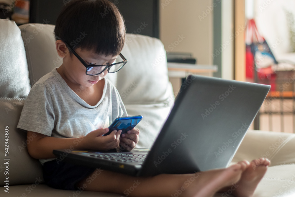 little boy Wear glass using laptop on sofa in home, work from home little boy Wear glass using laptop on sofa in home, work from home