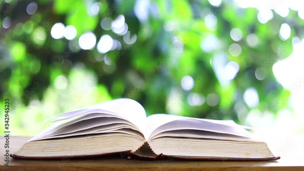 Books pages turning by wind on table in garden with bokeh background Books pages turning by wind on table in garden with bokeh background