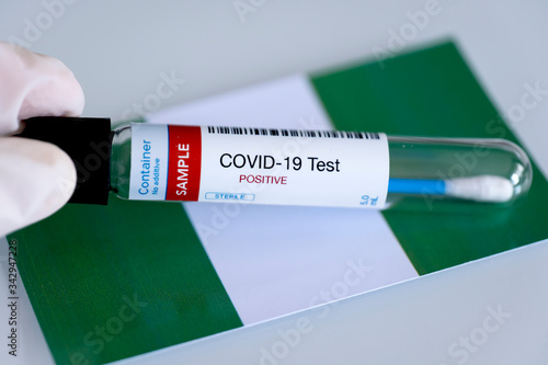 Testing for presence of coronavirus in Nigeria. Tube containing a swab sample that has tested positive for COVID-19. Nigerian flag in the background.