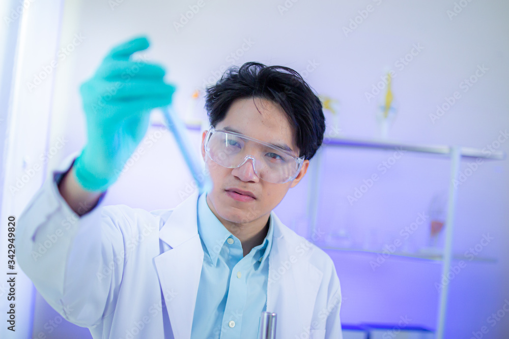 An Asian male scientist is watching blue liquid in a science test tube in a science lab. An Asian male scientist is watching blue liquid in a science test tube in a science lab.