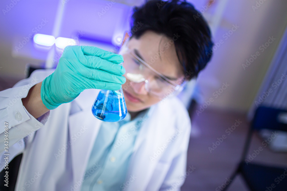 An Asian male scientist is watching blue liquid in a science test tube in a science lab. An Asian male scientist is watching blue liquid in a science test tube in a science lab.