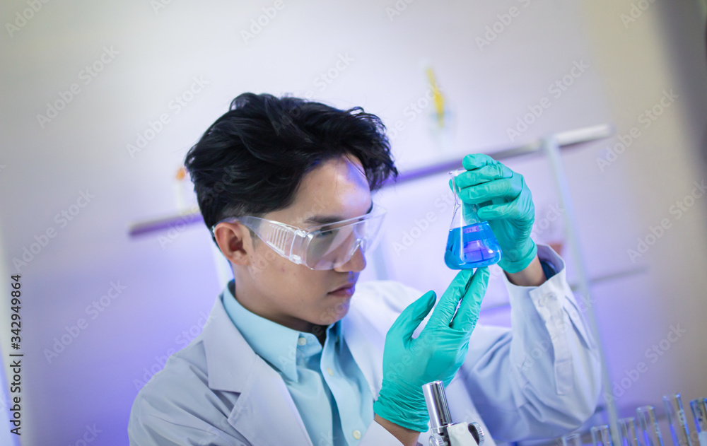 An Asian male scientist is watching blue liquid in a science test tube in a science lab. An Asian male scientist is watching blue liquid in a science test tube in a science lab.