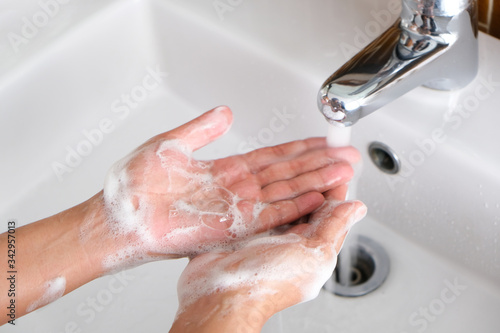 Hands of a beautiful woman wash their hands in a sink with foam to wash the skin and water flows through the hands. Concept of health, cleaning and preventing germs from contacting hands and beauty