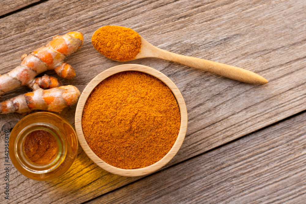 Tumeric powder ( curcumin, curcuma longa Linn) in wooden bowl and spoon with root and bottle of turmeric essential oil extracted isolated on old wood table background. Overhead view. Flat lay. Tumeric powder ( curcumin, curcuma longa Linn) in wooden bowl and spoon with root and bottle of turmeric essential oil extracted isolated on old wood table background. Overhead view. Flat lay.