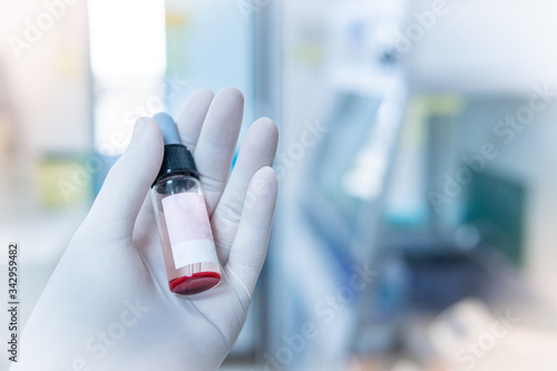 Fototapeta Naklejka Na Ścianę i Meble -  Close up of Hand wearing glove holding a Dropper Bottle blood test with blurred background, medical research lab and science laboratory concept.