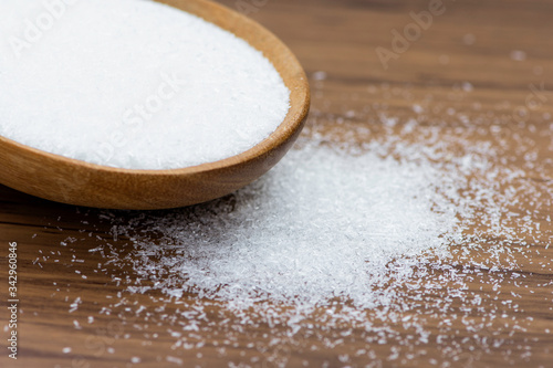 Monosodium glutamate ( MSG ) in wooden bowl pouring on rustic wooden table background.