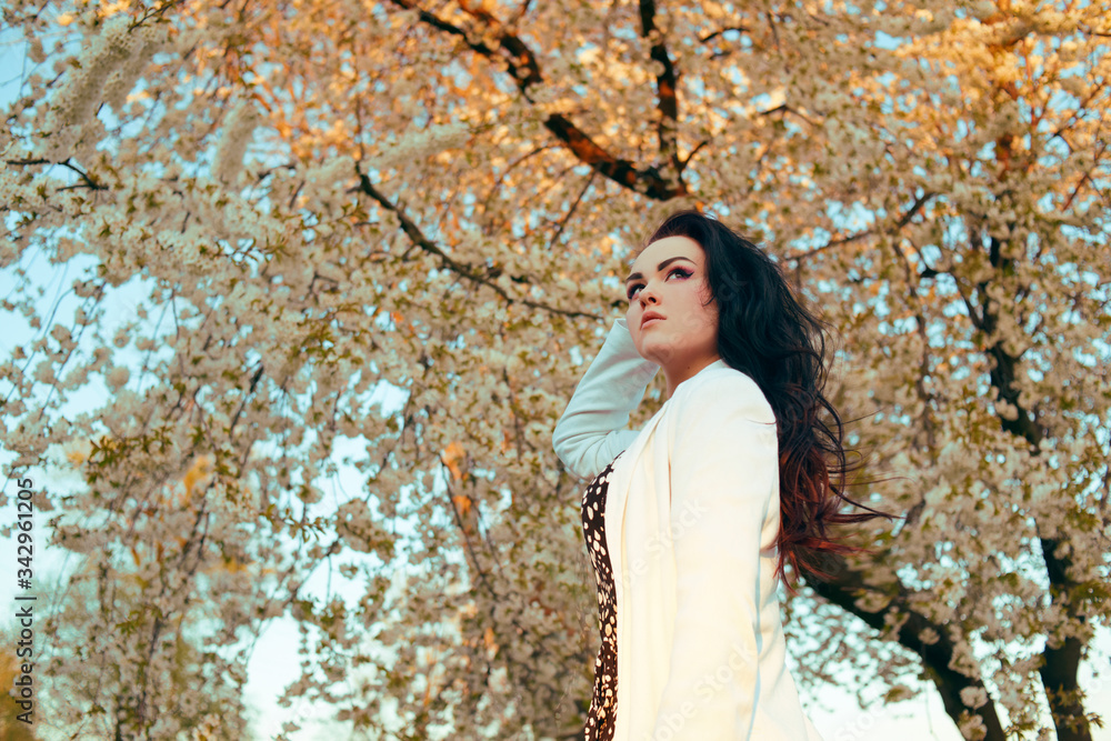 Fashionable stylishly dressed girl on a background of a tree with inflorescences, walks in the park on the street. Brunette model poses and enjoys nature. Spring Fashionable stylishly dressed girl on a background of a tree with inflorescences, walks in the park on the street. Brunette model poses and enjoys nature. Spring