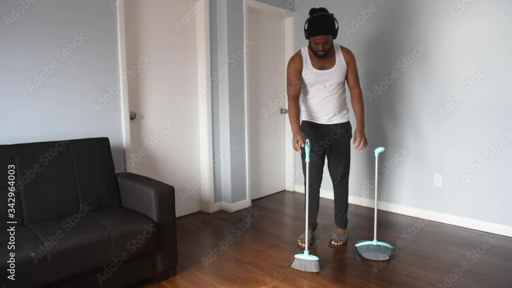Cool black man cleaning the house with broom. African american man on quarantine use broom to swep his flat. Funny concept Cool black man cleaning the house with broom. African american man on quarantine use broom to swep his flat. Funny concept