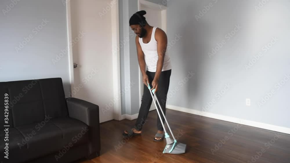 Cool black man cleaning the house with broom. African american man on quarantine use broom to swep his flat. Funny concept Cool black man cleaning the house with broom. African american man on quarantine use broom to swep his flat. Funny concept