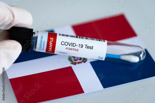 Testing for presence of coronavirus. Tube containing a swab sample that has tested positive for COVID-19. Dominican Republic flag in the background.