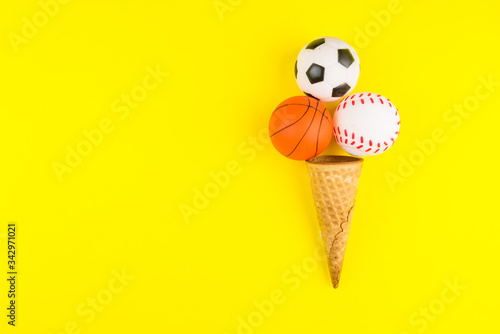 Fototapeta Naklejka Na Ścianę i Meble -  Sport ball toys in ice cream waffle cone on yellow background in minimal style. Concept sports entertainment. Top view Copy space Template for text or your design.