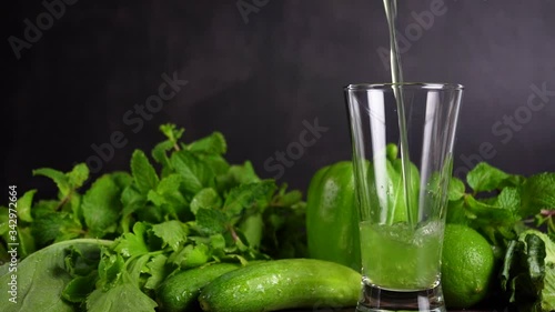 Pouring mixed green vegetables with fruits juice into a glass and fresh vegetables background. Slow motion.
