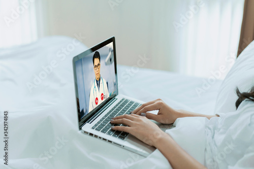 Asia Chinese male doctor video conference call online lives to talk remotely medical coronavirus result with Asian woman on bedroom couch at home. Online healthcare digital technology service concept