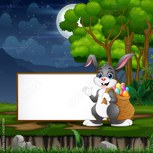 Easter bunny carrying a sack of easter eggs in front the blank sign