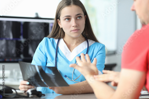 Close-up of serious doctor listening to patient. Young concentrated female wearing uniform and professional equipment stethoscope. Modern medicine and x ray concept