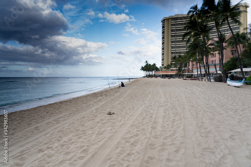 Waikiki Beach Hawaii opening day of the COVID pandemic. Few people, lone fisherman, diamond head, nearly empty beach a rainbow saying the beach is open.
