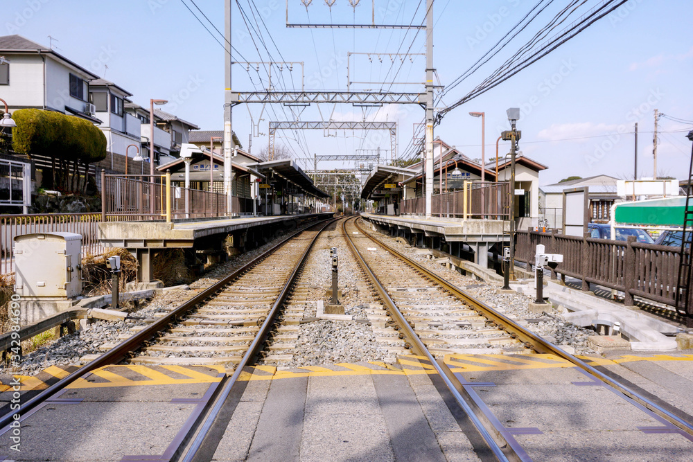 Perspective and outside view of railroad crossing with railroad track and long shot of people waiting to a train at Nara train platform on blue sky background.