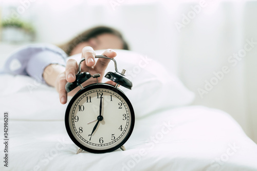 Quarantine. hand of young woman sleeping on bed pressing snooze button on black vintage alarm clock at seven o'clock morning in bed room at home, lifestyle, good morning and healthy sleep concept
