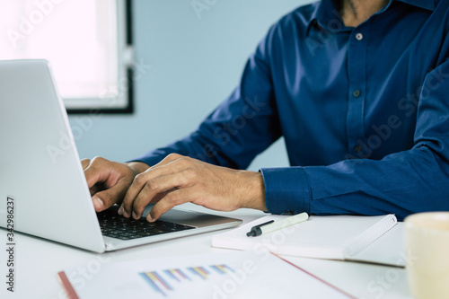 businessman working on laptop computer with graph chart, document report, notebook and coffee cup on desk at home, work from home, quarantine, accountant and business finance technology concept