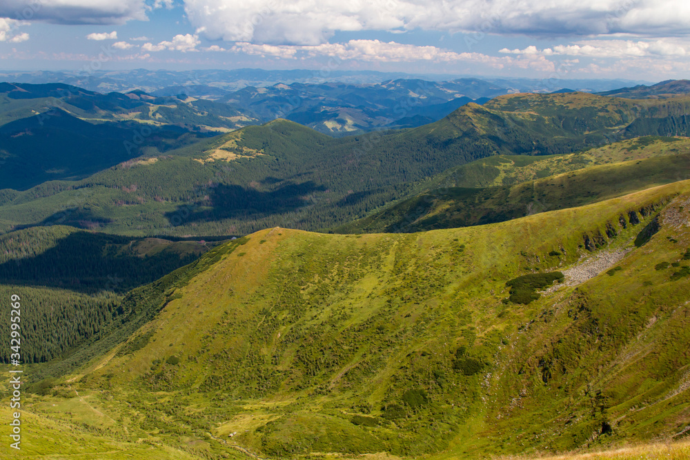 Landscape of mountain ranges and slopes. Meadows in the mountains in rays of the summer sun breaking through the clouds in the summer in the middle of the day. Carpathians
