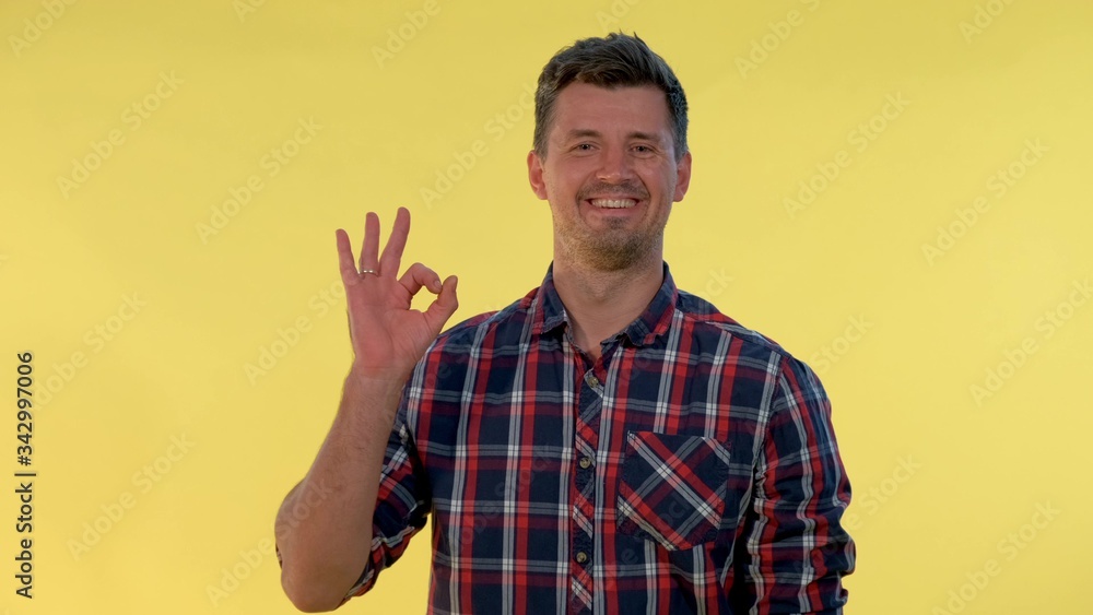 Attractive young man making 'okay' hand sign. He making hand gesture on yellow background. Attractive young man making 'okay' hand sign. He making hand gesture on yellow background.