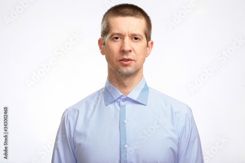 A handsome serious man in a blue shirt looks into the camera. Isolated