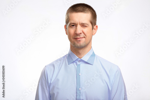 confident successful winking man closed one eye, wearing a blue shirt, staring at the camera. Isolated