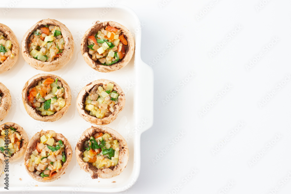 Caps of champignon mushrooms stuffed with vegetables on a white plate. Cooking process. Prepared for baking. Top view. Caps of champignon mushrooms stuffed with vegetables on a white plate. Cooking process. Prepared for baking. Top view.