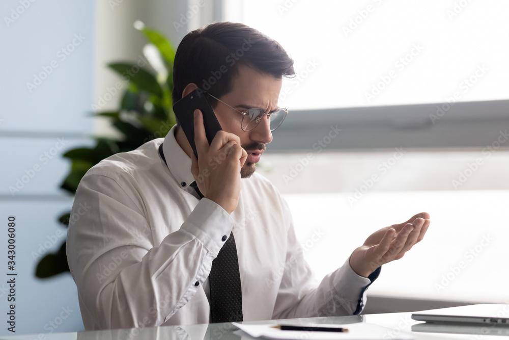 Frustrated businessman angry over bad news message talking on smartphone. Unhappy man employee argue using modern cell phone. Male customer dissatisfied and shocked by service in office. Frustrated businessman angry over bad news message talking on smartphone. Unhappy man employee argue using modern cell phone. Male customer dissatisfied and shocked by service in office.