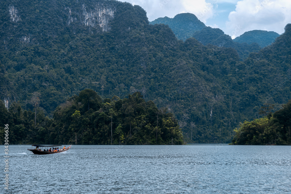 Boat with tourists on the background of a tropical landscape. Green mountains and lake. Khao Sok National Park and Cheo Lan Lake. Thailand