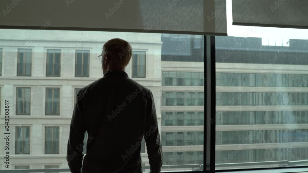 a man in the office looks out the window at the city a man in the office looks out the window at the city