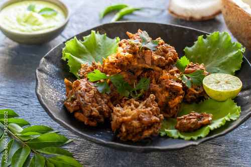 Indian cuisine Indian food. pakora traditional Indian deep-fried snack. pakoras on black plate with coconut chutney sauce curry leaves. national appetiser authentic vegetarian Asian food. travel food