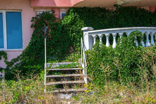 Abandoned hotel on the beach, covered in green grass and climbing ivy plant, nature take over concept, building facade