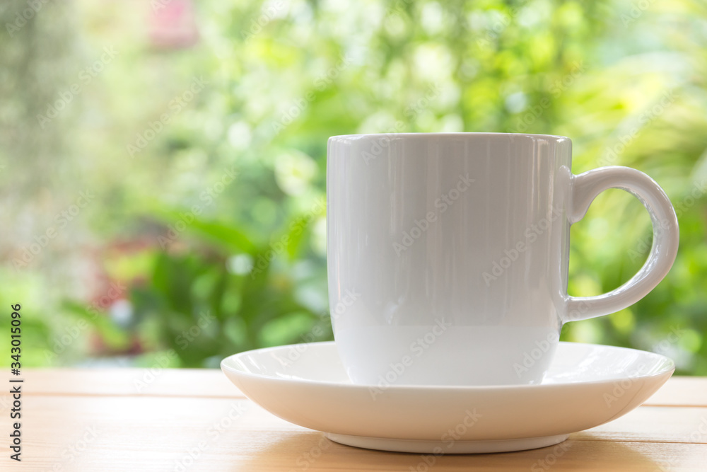 White coffee mug on wooden space background, Back is a tree with a refreshing morning light. White coffee mug on wooden space background, Back is a tree with a refreshing morning light.