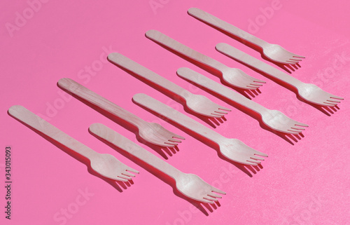 Many eco-friendly wooden forks on pink background. Minimalistic eco concept. Pop art