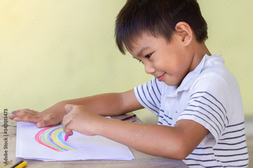 Selective focus. Happy Asian child boy drawing and coloring the rainbow. Study and stay at home concept. Learning and education. Portrait image of 5-6 years old boy. Selective focus. Happy Asian child boy drawing and coloring the rainbow. Study and stay at home concept. Learning and education. Portrait image of 5-6 years old boy.