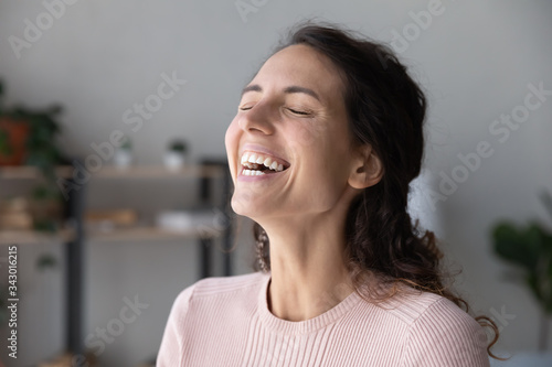 Close up head shot overjoyed healthy young attractive woman laughing at funny joke. Emotional sincere pretty millennial girl feeling excited indoors, good mood, positive feature of character concept.