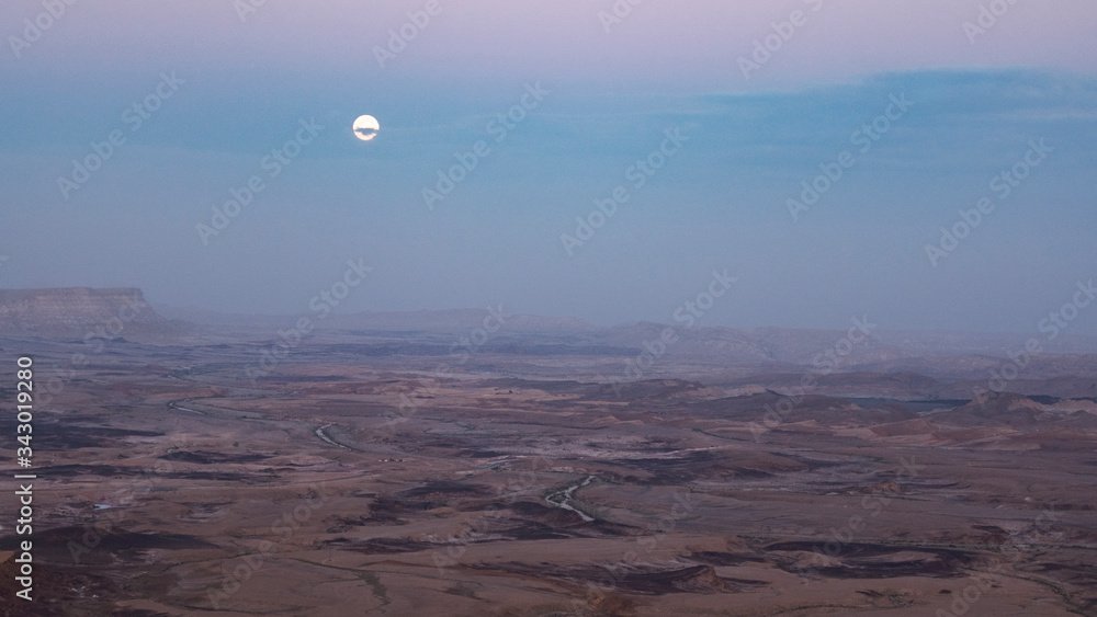 full moon peaking through clouds above the makhtesh ramon crater in israel just after sunset in mitzpe ramon in israel full moon peaking through clouds above the makhtesh ramon crater in israel just after sunset in mitzpe ramon in israel