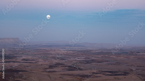 full moon peaking through clouds above the makhtesh ramon crater in israel just after sunset in mitzpe ramon in israel