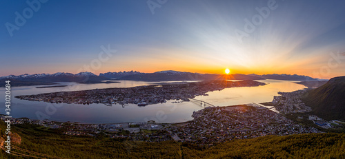 Panoramic view of the city of Tromso  located in Northern Norway. Various city landmarks are visible  with the midnight sun setting over the landscape in the background.