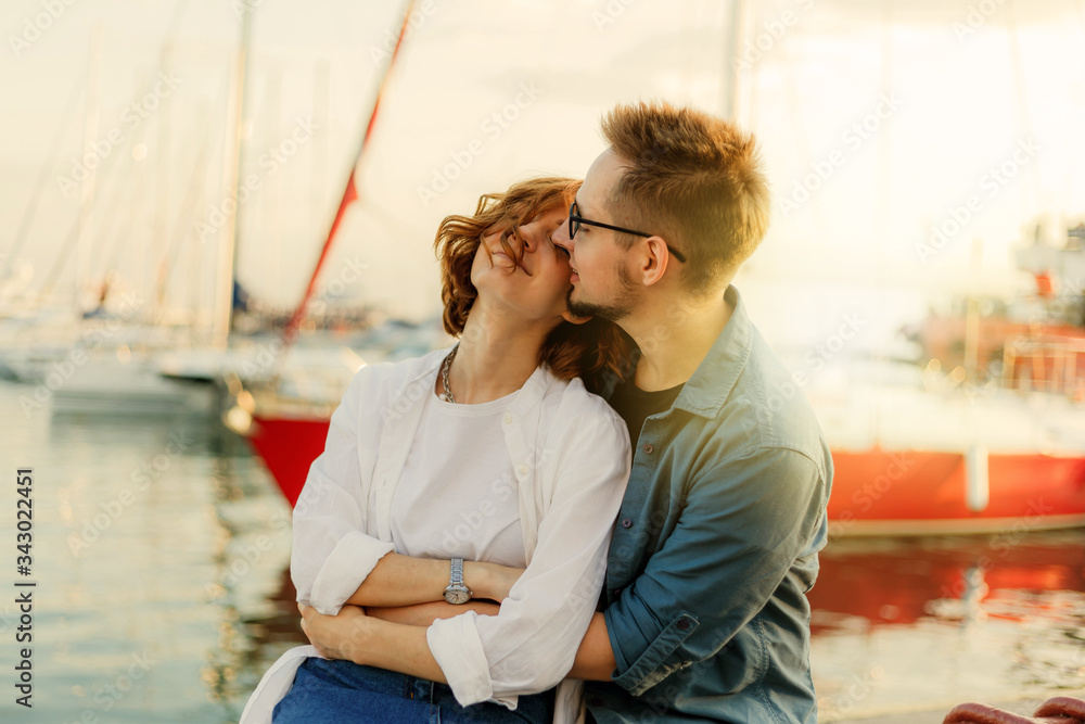 Loving cheerful couple of lovers sitting on a bench against the background of yachts club at sea. Romantic, love story concept