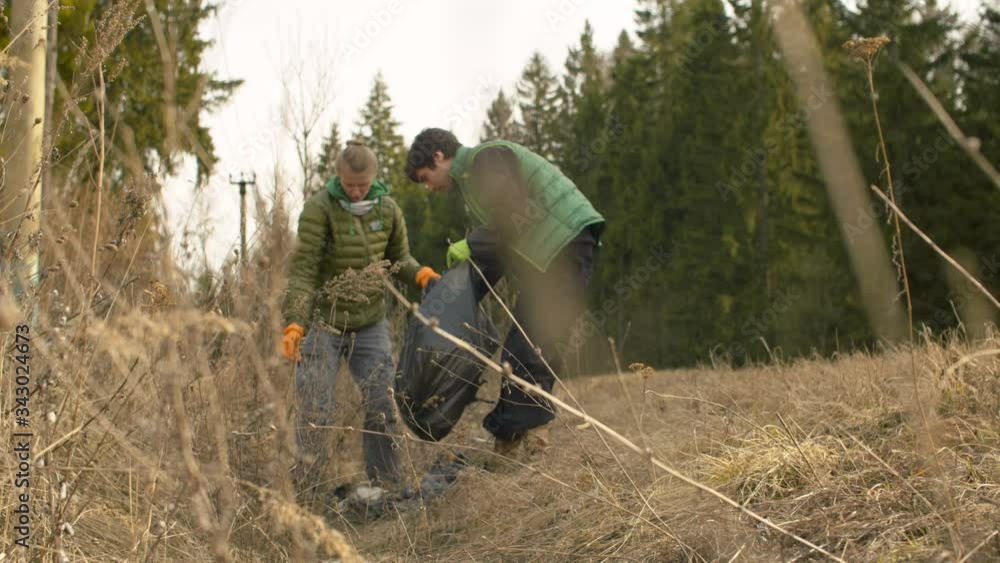 Young couple eco volunteers collecting garbage on the road near the forest in spring. Green conifers trees, last years dry grass. Earth day, eco friendly concept Young couple eco volunteers collecting garbage on the road near the forest in spring. Green conifers trees, last years dry grass. Earth day, eco friendly concept