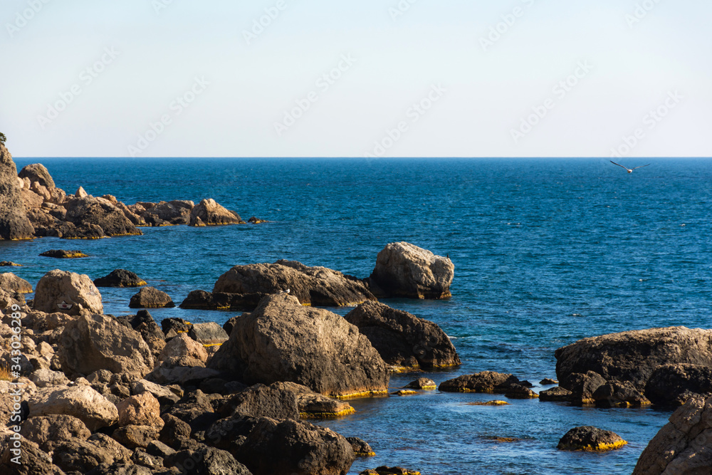 View of the sea waves and fantastic rocky coast. View of calm turquoise sea water and rocks. Drawing of the sea surface and rocky coast. Rocky coast of the Peninsula